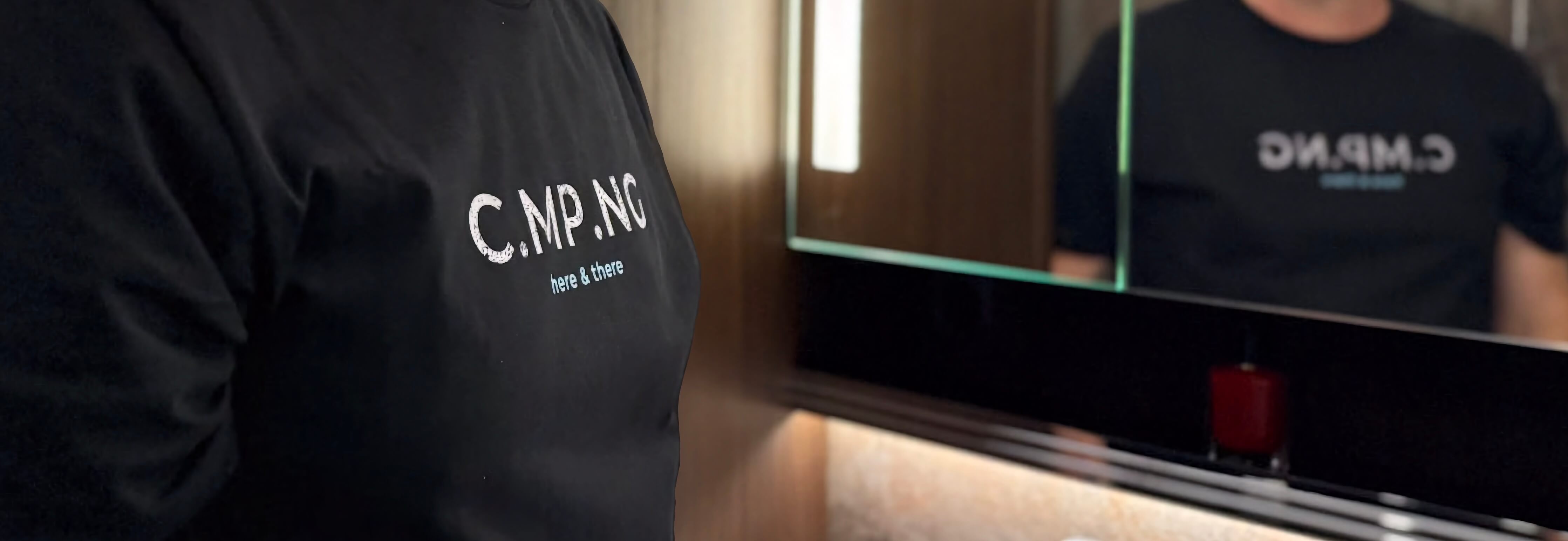 Ein Mann steht mit seinem C.MP.NG T-Shirt in einem Wohnmobil vor einem Spiegel.