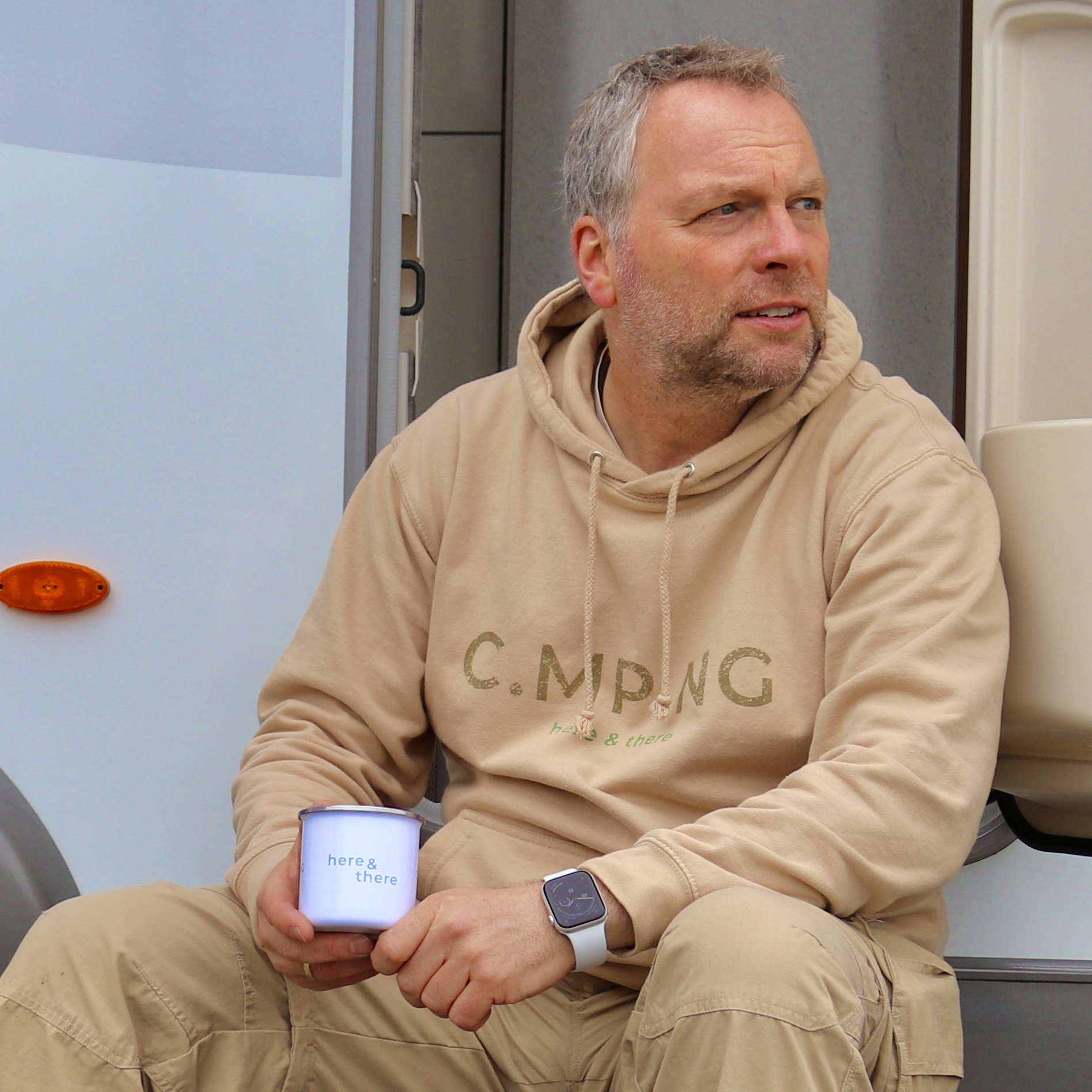 Ein Mann sitzt vor einem Wohnmobil mit einem Camping Hoodie von C.MP.NG