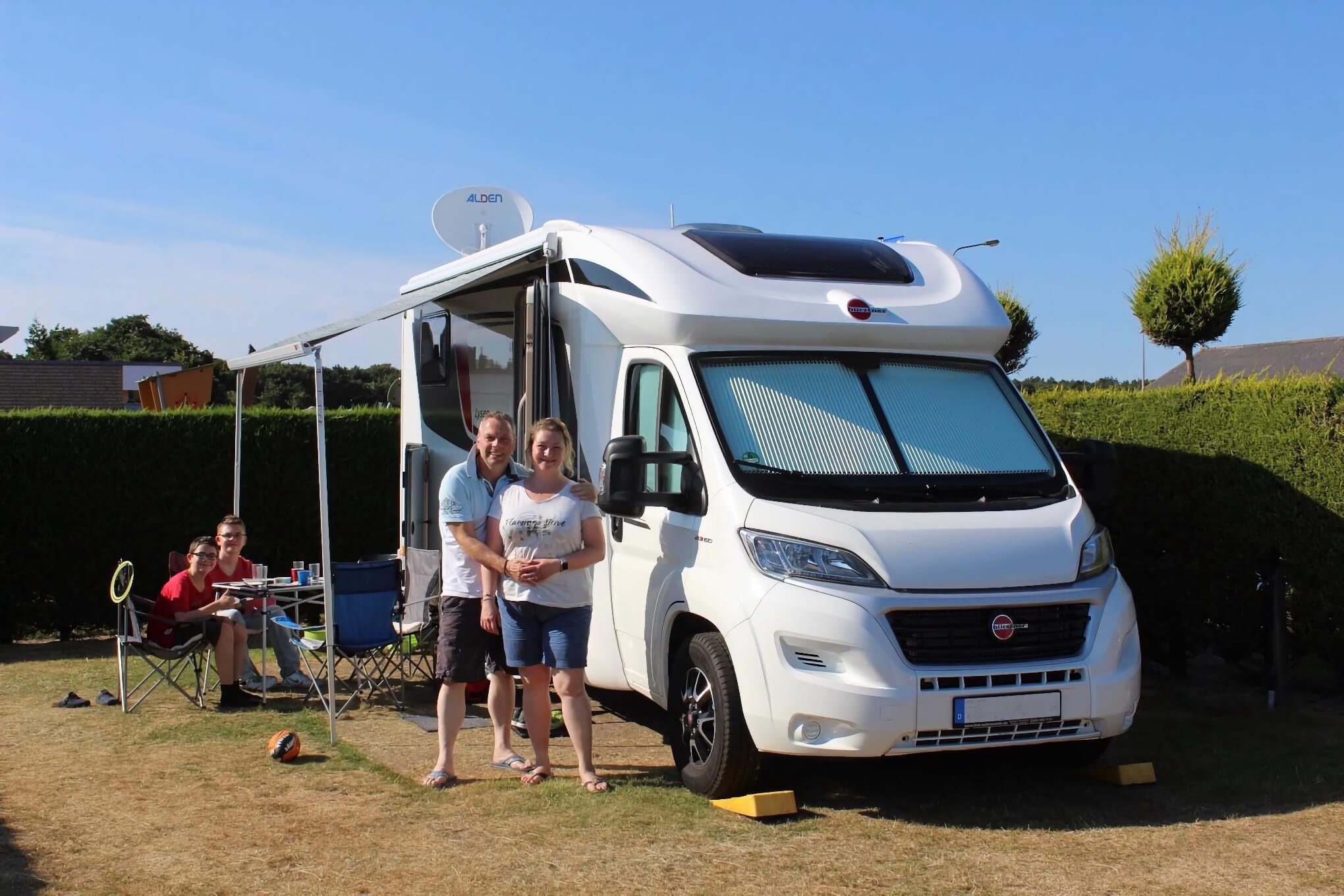 Eine Vierköpfige Familie steht vor einem Camping Mobil mit C.MP.NG Camping Aufkleber. 